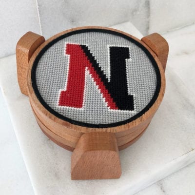 A wooden coaster with a cross stitch letter n on it.