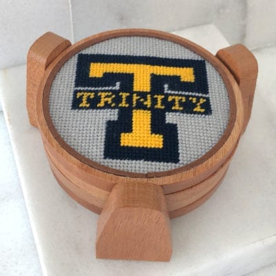 A cross stitch of the letter t on top of a wooden coaster.