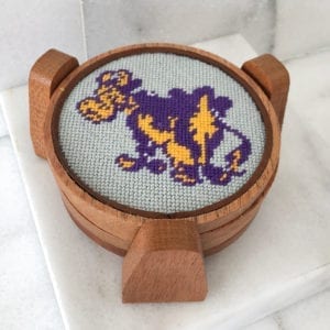 A wooden coaster with a cross stitch design on it.