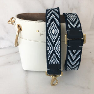 A white purse and black strap with an ornament on it.