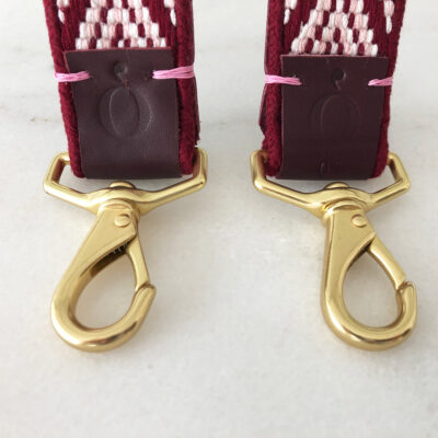 A pair of gold hooks holding up two maroon and white straps.