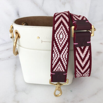 A white purse with a maroon strap on it