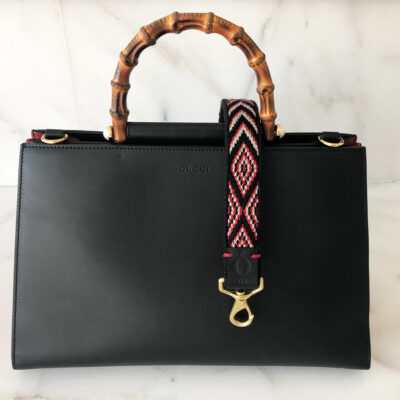A black purse with bamboo handles and a red strap.
