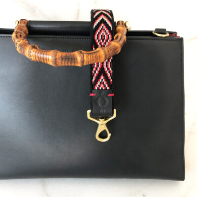 A black purse with a wooden handle and a red, white and blue strap.