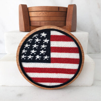 A round wooden frame with an american flag stitched on it.