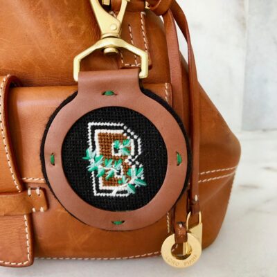 A brown purse with a green and black cross stitch design on it.