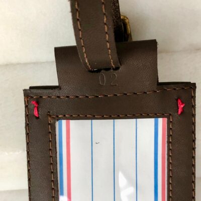 A brown leather luggage tag with red, blue and white lines.
