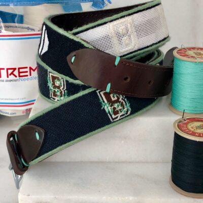 A belt with a brown leather strap and some green thread